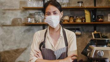 Portrait young Asia girl waitress wear medical face mask feeling happy smile waiting for clients after lockdown at urban cafe. Owner small business, food and drink, business reopen again concept. photo