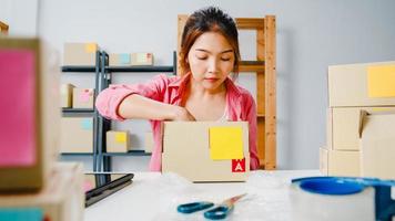 Young Asia entrepreneur businesswoman packing product in cardboard box deliver to customer, working at home office. Small business owner, start up online market delivery, lifestyle freelance concept.