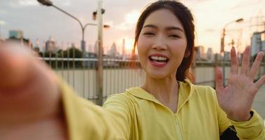 Attractive young Asia athlete influencer lady recording video vlog live streaming on phone upload in social media while exercises in urban city. Sportwoman wearing sports clothes on street in morning. photo