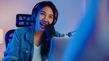 feliz asia girl host record podcast use micrófono use auriculares con laptop entrevista invitada conversación para contenido en su estudio en casa por la noche. concepto de equipo de sonido. concepto de creador de contenido. foto