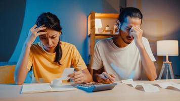 Stress asia couple man and woman use calculator for calculate family budget, debts, expenses during financial economic crisis at home at night. Marriage money trouble, Family budget plan concept. photo