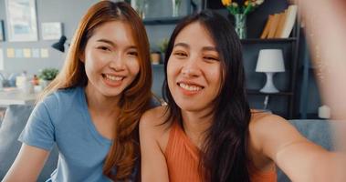 Teenager Asian women feeling happy smiling selfie and looking to camera while relax in living room at home. Cheerful Roommate ladies video call with friend and family, Lifestyle woman at home concept. photo