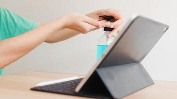 Asian woman using alcohol gel sanitizer wash hand before using tablet for protect coronavirus. Female push alcohol to clean for hygiene when social distancing stay at home and self quarantine time. photo