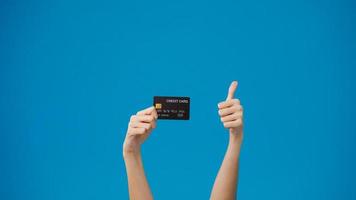 Young girl hold in hand credit bank card showing thumb up isolated over blue background in studio. Copy space for place a text, message for advertisement. Advertising area, mockup promotional content. photo