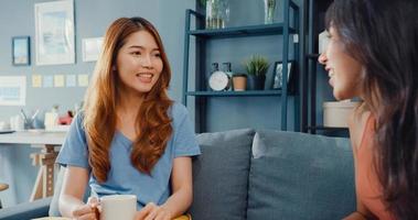 Asia housewife women with casual relax on couch with cup of tea talk together about their life and husband relationship gossip in living room at house. Girls friends roommate stay in dorm together. photo