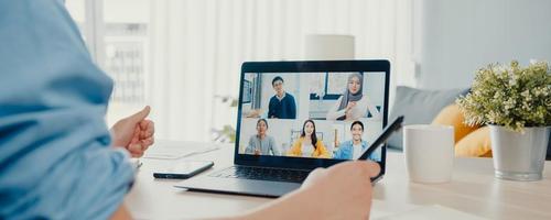 Young Asia businessman using laptop talk to colleagues about plan in video call meeting work from home at living room. Self-isolation, social distance, panoramic banner background with copy space. photo