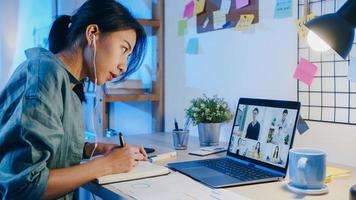 Asia empresaria usando laptop hablar con colegas sobre el plan en la reunión de videollamada en la sala de estar. trabajando desde casa por sobrecarga nocturna, trabajo a distancia, distanciamiento social, cuarentena por coronavirus. foto