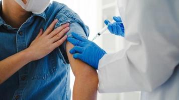 Young Asia lady doctor giving Covid-19 or flu antivirus vaccine shot to senior male patient wear face mask protection from virus disease at health clinic or hospital office. Vaccination concept. photo