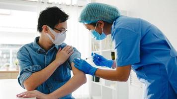 Young Asia lady nurse giving Covid-19 or flu antivirus vaccine shot to senior male patient wear face mask protection from virus disease at health clinic or hospital office. Vaccination concept. photo