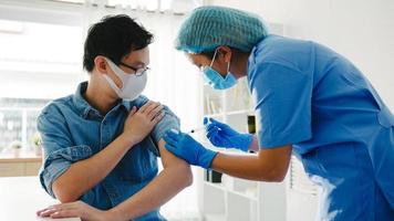 joven enfermera de asia dando covid-19 o vacuna antivirus contra la gripe inyectada a un paciente masculino mayor que usa protección de máscara facial contra la enfermedad del virus en la clínica de salud o en la oficina del hospital. concepto de vacunación. foto