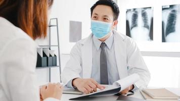 Serious Asia male doctor wear protective mask using clipboard is delivering great news talk discuss results or symptoms with female patient in hospital office. Lifestyle new normal after corona virus. photo