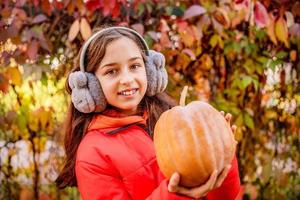 Autumn portrait of a little girl in an orange jacket with a pumpkin in her hands. The girl smiles. photo