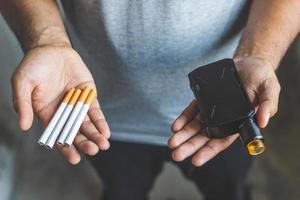 Young man holding electronic cigarette and cigarette.