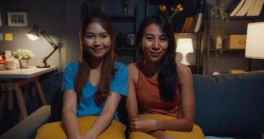 Teenager Asia women feeling happy smiling and looking to camera while relax in living room at home night. Cheerful Roommate ladies video call with friend and family, Lifestyle woman at home concept. photo