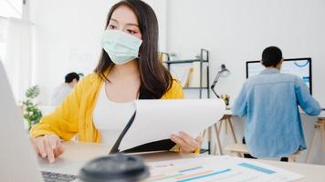 Asia businesswoman entrepreneur wearing medical face mask for social distancing in new normal situation for virus prevention while using laptop back at work in office. Lifestyle after corona virus. photo