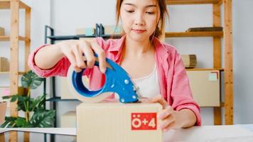 Young Asia entrepreneur businesswoman packing product in cardboard box deliver to customer, working at home office. Small business owner, start up online market delivery, lifestyle freelance concept. photo