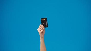 Young woman hand shows credit card for shopping online over blue background in studio. Copy space for place a text, message for advertisement. Advertising area, mockup promotional content. photo