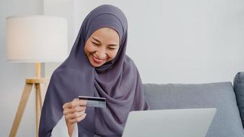 Señora musulmana de Asia que usa la computadora portátil, compra con tarjeta de crédito y compra Internet de comercio electrónico en la sala de estar de la casa. quedarse en casa, compras en línea, autoaislamiento, distanciamiento social, cuarentena por coronavirus. foto