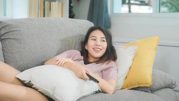 Joven mujer asiática adolescente viendo la televisión en casa, mujer sintiéndose feliz acostado en el sofá en la sala de estar. mujer de estilo de vida relajarse por la mañana en el concepto de hogar. foto