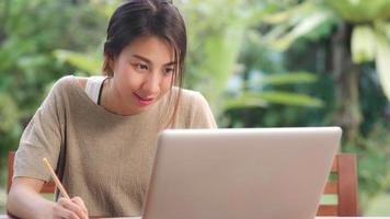 Freelance Asian woman working at home, business female working on laptop sitting on table in the garden in morning. Lifestyle women working at home concept. photo