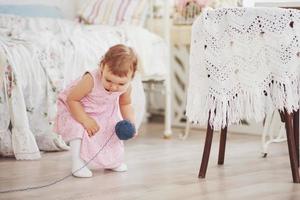 Childhood concept. Baby girl in cute dress play with colored thread. White vintage childroom photo