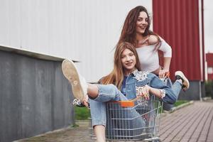 dos jóvenes mujeres felices que se divierten carrera de carritos de compras al aire libre. foto