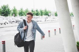 joven apuesto con una bolsa al hombro a toda prisa hacia el aeropuerto. foto