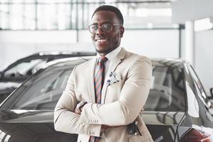 Young black businessman on auto salon background. Car sale and rent concept photo