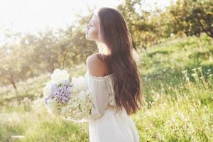A beautiful young girl in a white light dress and a bouquet of summer flowers lays a fine day in the garden photo
