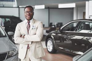 joven empresario negro en el fondo del salón del automóvil. concepto de venta y alquiler de coches