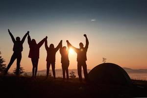 Una silueta de un grupo de personas se divierte en la cima de la montaña cerca de la carpa durante la puesta de sol. foto