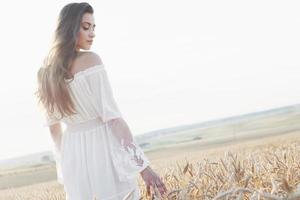 Hermosa chica en vestido blanco corriendo en el campo de trigo de otoño al atardecer foto
