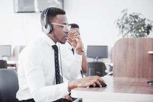 Operador de soporte al cliente afroamericano con auriculares manos libres trabajando en la oficina foto