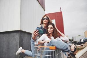 dos jóvenes mujeres felices que se divierten carrera de carritos de compras al aire libre. foto