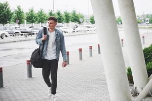 joven apuesto con una bolsa al hombro a toda prisa hacia el aeropuerto. foto