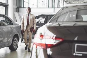 Young black businessman on auto salon background. Car sale and rent concept photo