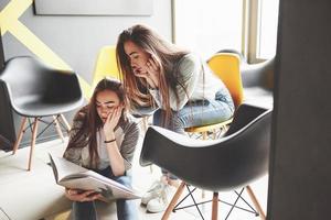Two beautiful twin girls spend time read a book in library in the morning. Sisters relaxing in a cafe and having fun together photo