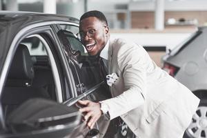 Hombre africano mirando un coche nuevo en el concesionario de coches.