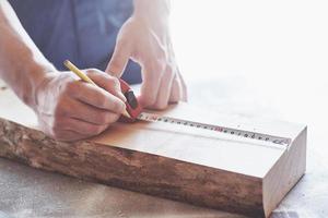 A carpenter in working clothes and a small business owner takes a wooden board with a ruler and pencil. photo