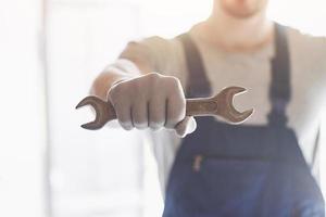 Hand in gloves with a metal wrench on a background of a worker's costume factory. photo