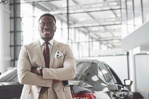 joven empresario negro en el fondo del salón del automóvil. concepto de venta y alquiler de coches