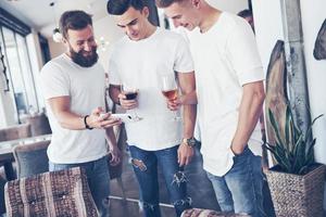 Cheerful old friends communicate with each other and phone watch, with glasses of whiskey or wine in pub. Concept of entertainment and lifestyle. Wifi connected people in bar table meeting photo