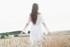 Sensible joven vestida de blanco posando en un campo de trigo dorado foto