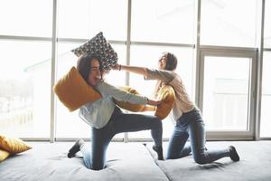 Two beautiful young twins sisters spending time together and are battling with pillows. Siblings having fun at home concept photo