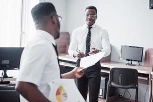 discutir un proyecto. Dos hombres de negocios negros en ropa formal discutiendo algo mientras uno de ellos apunta un papel foto