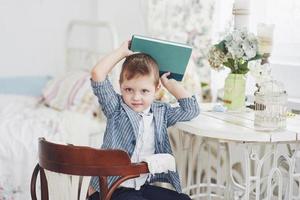 Photo of diligent schoolboy with book on his head does not want to study and go to school. The schoolboy is tired of doing homework