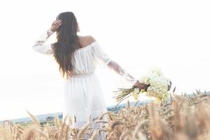 Sensible joven vestida de blanco posando en un campo de trigo dorado