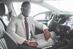 elegante hombre de negocios negro sentado al volante del nuevo coche de lujo. rico hombre afroamericano foto