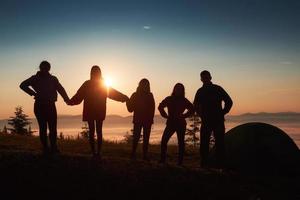 Una silueta de un grupo de personas se divierte en la cima de la montaña cerca de la carpa durante la puesta de sol. foto