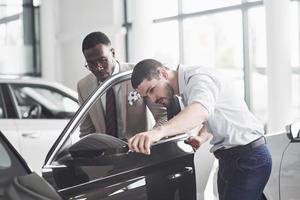 un hombre africano que compra un automóvil nuevo revisa un automóvil hablando con un proveedor profesional. foto